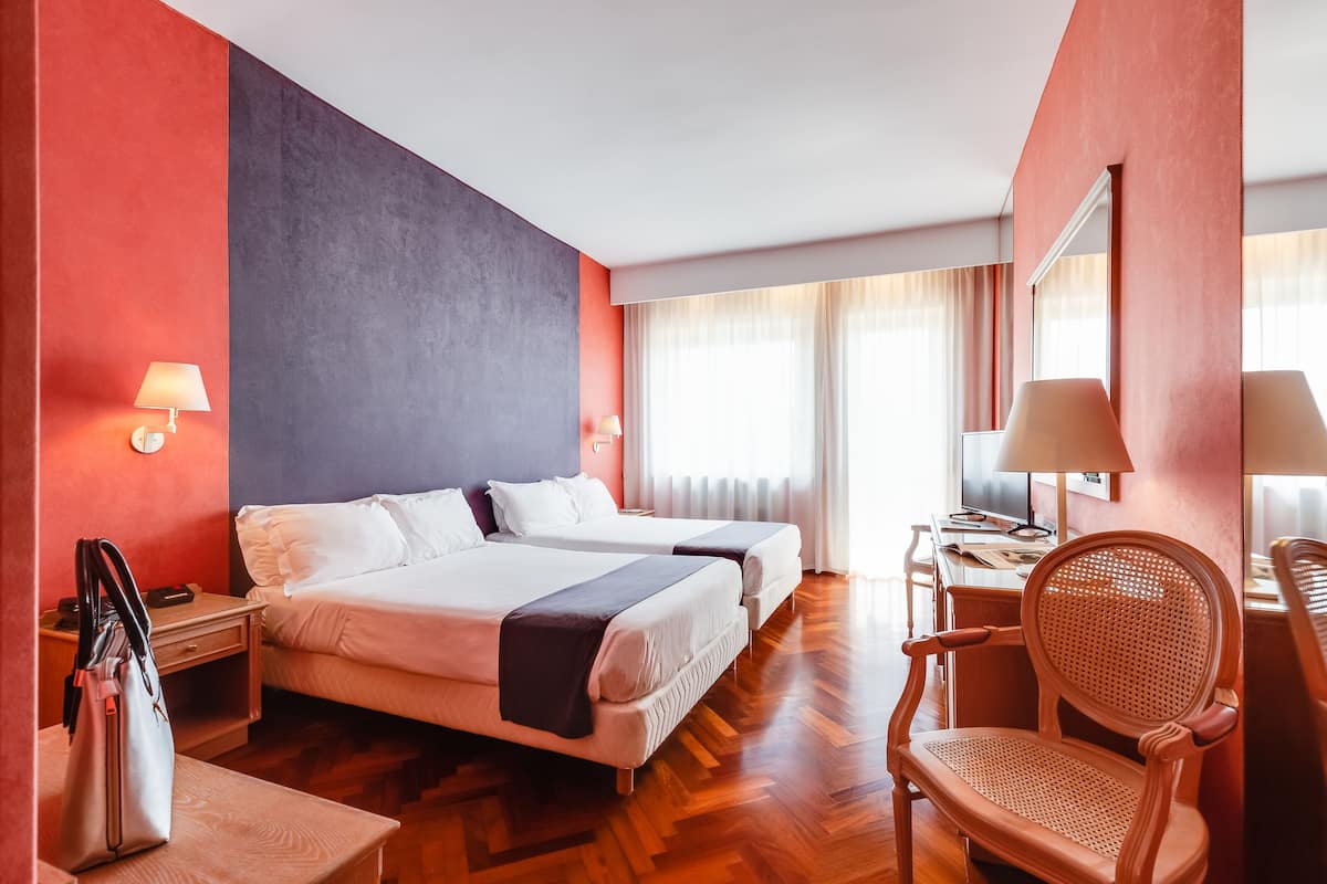 A hotel room with two beds, a desk, a chair, and a large mirror.