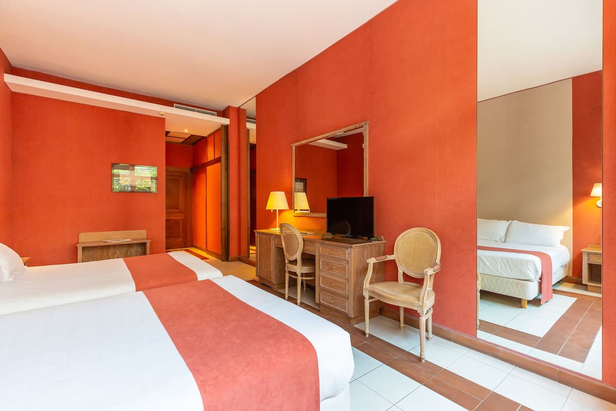 A hotel room with two beds, a desk with a chair, a television, and a large mirror.