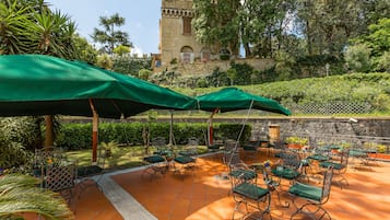 An outdoor patio with green umbrellas, metal chairs, and a stone wall.