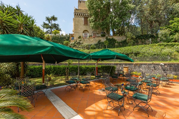 An outdoor patio with green umbrellas, metal chairs, and a stone wall.