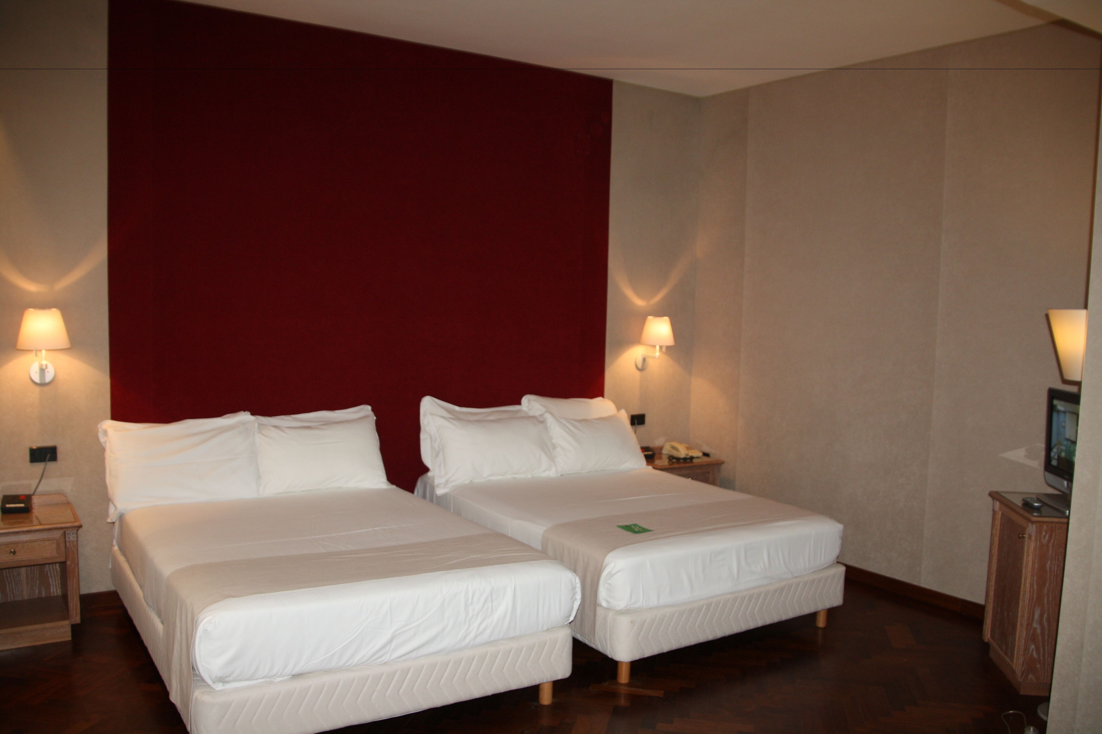A hotel room with two beds, a red accent wall, and bedside lamps.
