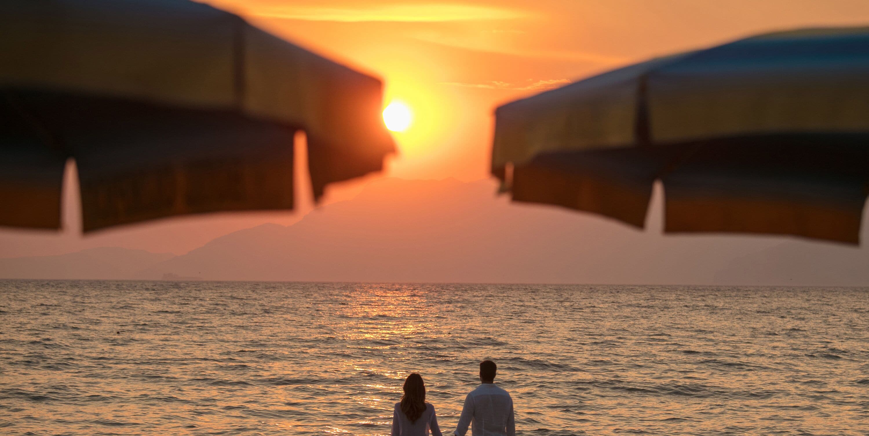 Een zonsondergang boven de oceaan, een koppel staat op het strand.