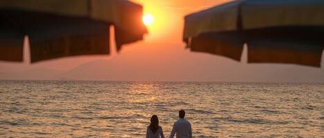 Una puesta de sol sobre el océano con una pareja de pie en la orilla.