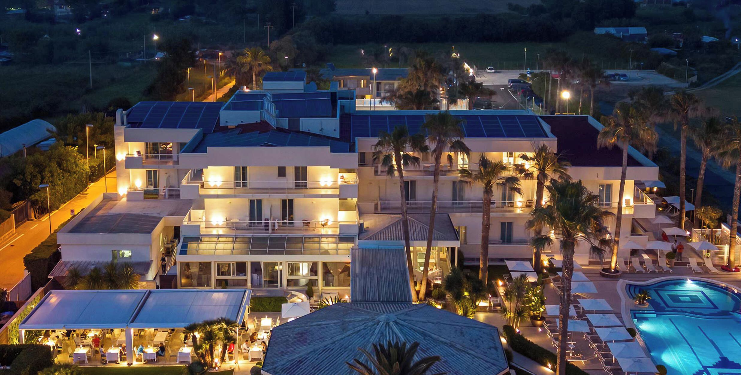 A multi-story hotel with a pool, outdoor seating, and solar panels.