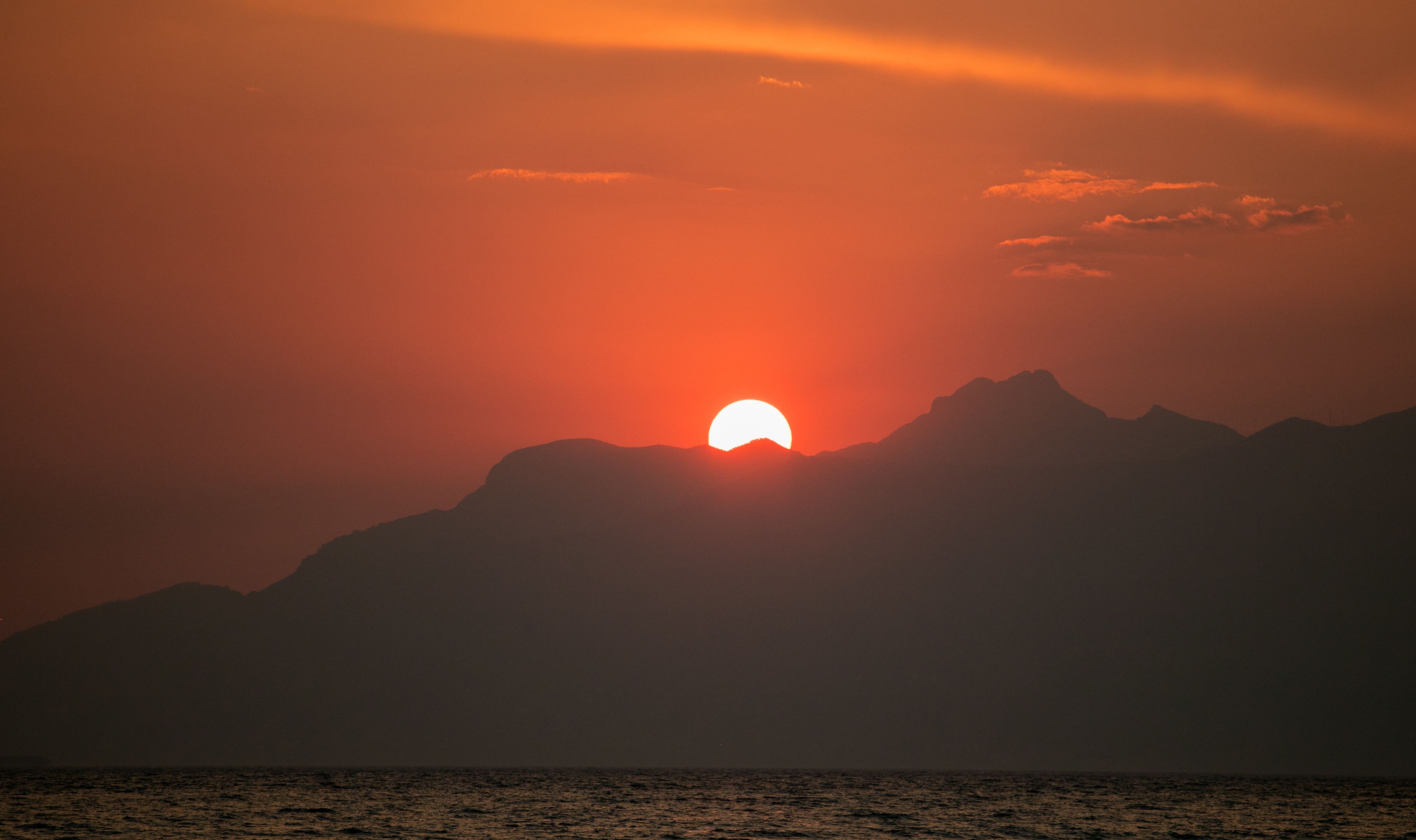 A sunset over a mountain range with a body of water in the foreground.