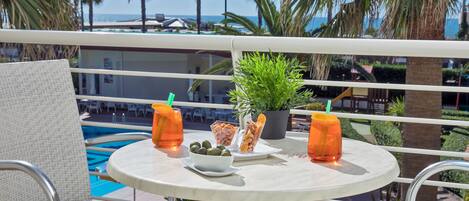 A round table with a white tablecloth, two orange drinks, a bowl of olives, a potted plant, and a plate of snacks.