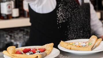 A person sprinkling powdered sugar over a dessert plate with a crepe and strawberries.