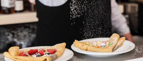 Une personne saupoudre du sucre glace sur une assiette de dessert contenant une crêpe et des fraises.