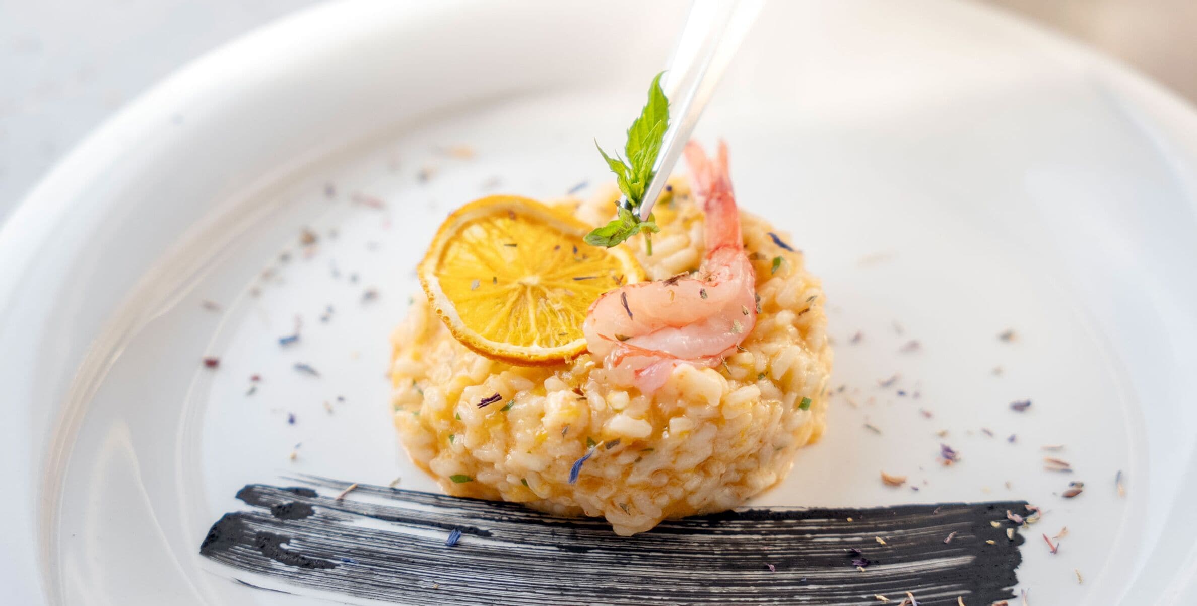 A plate of risotto with shrimp and a lemon slice garnish.