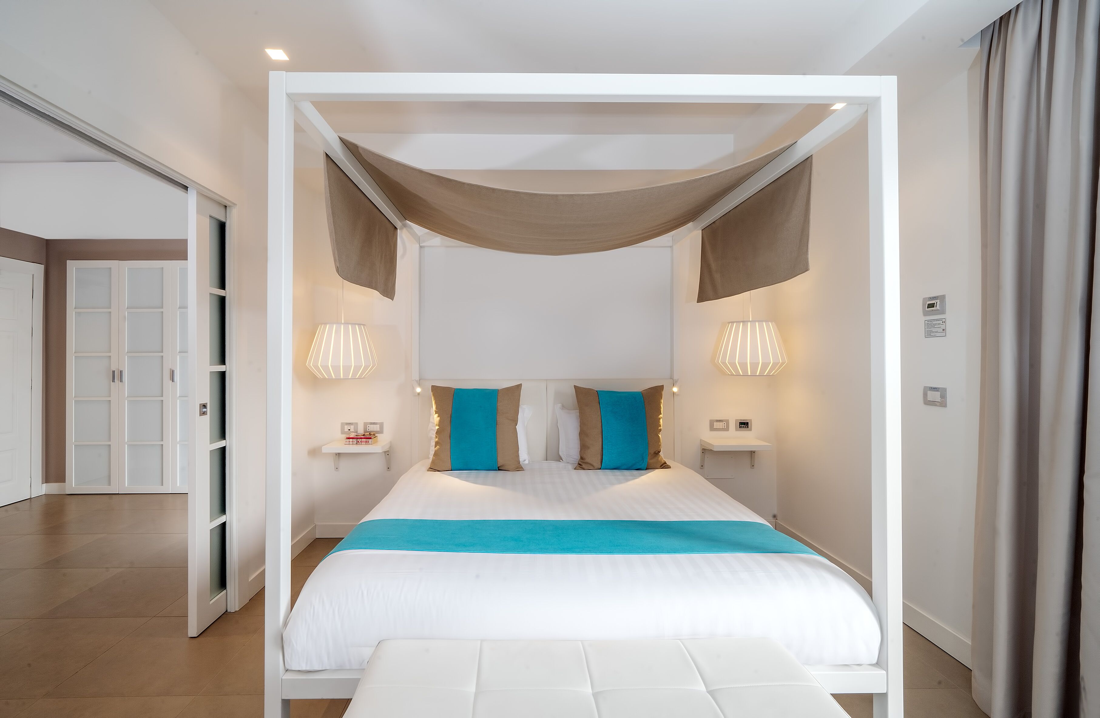 Un dormitorio moderno con cama a dosel, lámparas de noche y una paleta de colores neutros.