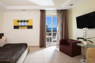 A hotel room with a bed, a TV, a sofa, and a balcony with a view of the sea.