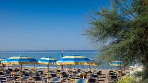 A beach with rows of sun loungers and blue and yellow striped umbrellas. - Hotel Olimpico (Pontecagnano Faiano)