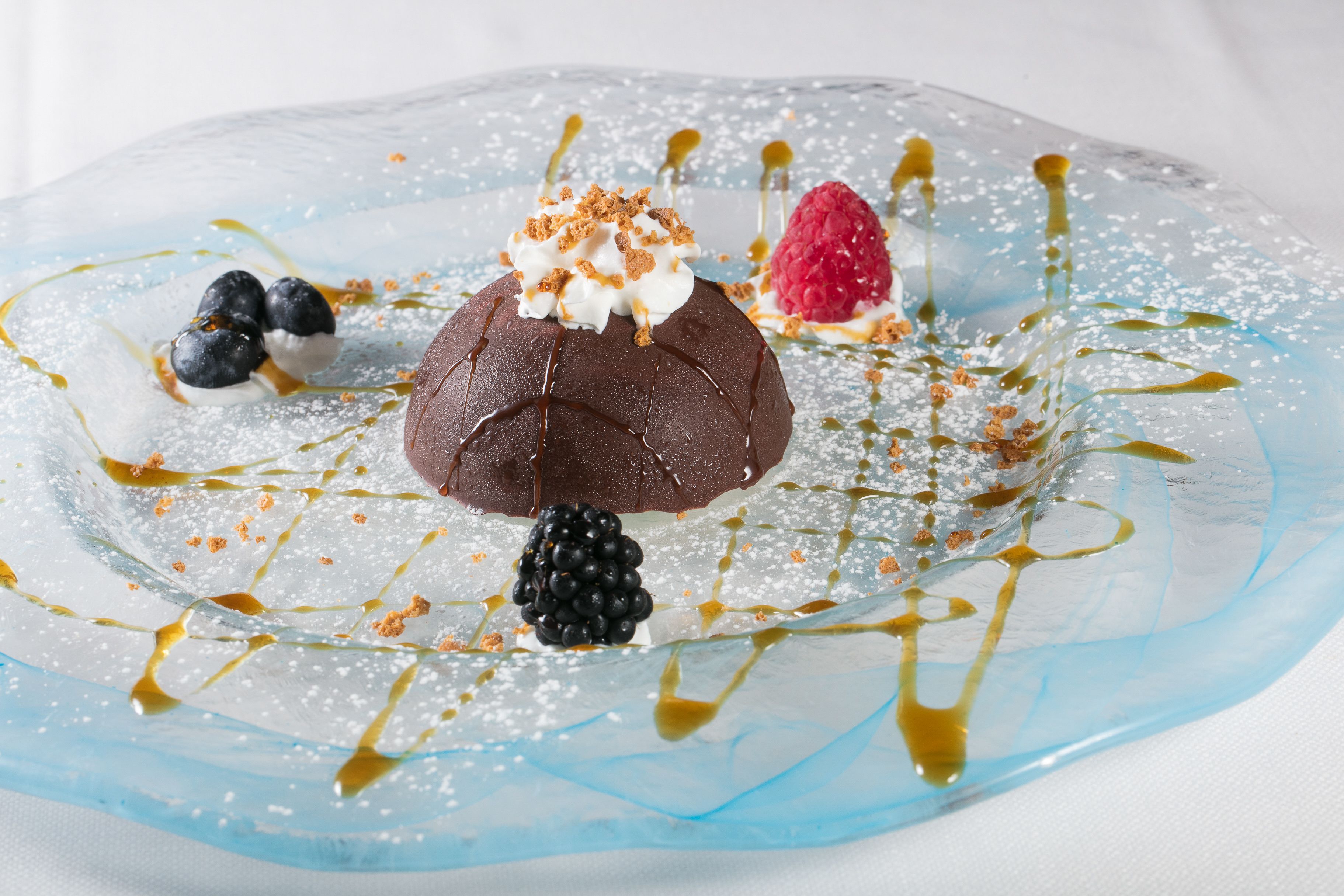 A dessert with chocolate, berries, and caramel sauce on a clear glass plate.