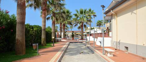 A courtyard with a croquet field, palm trees, and a building with a balcony.