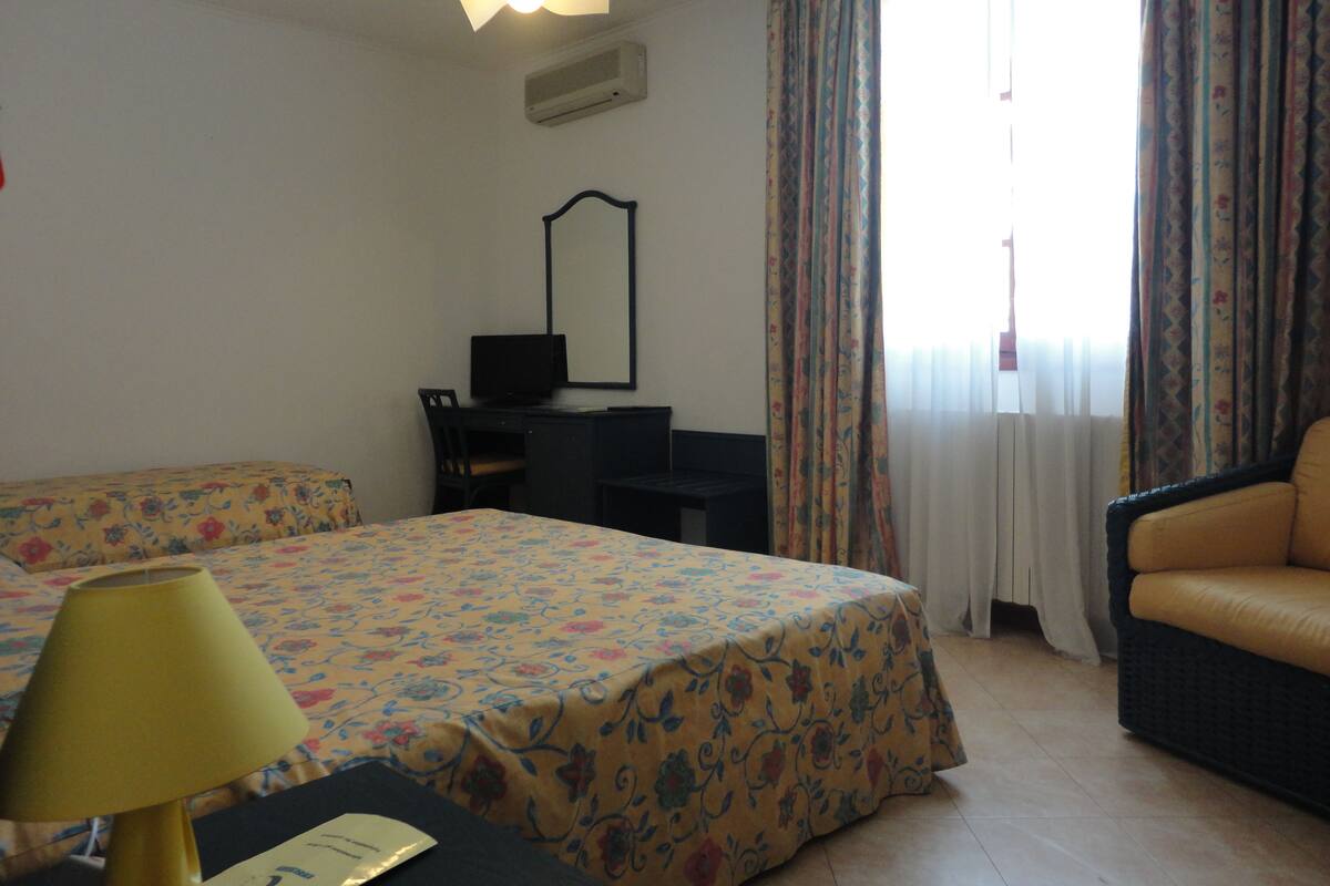 Ein Hotelzimmer mit Bett, Schreibtisch, Stuhl, Lampe und einem Fenster mit Vorhängen.