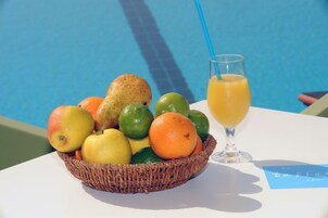 Un cesto di frutta con mele, arance e lime accanto a un bicchiere di succo d'arancia vicino a una piscina.