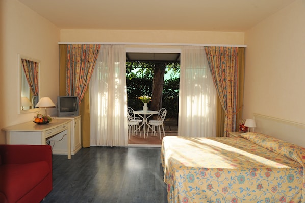 Une chambre d’hôtel comprenant un lit, un bureau avec une télévision, un fauteuil rouge, une table à manger avec des chaises et une vue sur l’extérieur grâce à une porte coulissante.