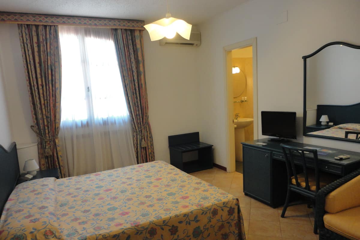 Ein Hotelzimmer mit Bett, Schreibtisch, Stuhl, Spiegel und einem durchgegangenen Tür sichtbaren Badezimmer.