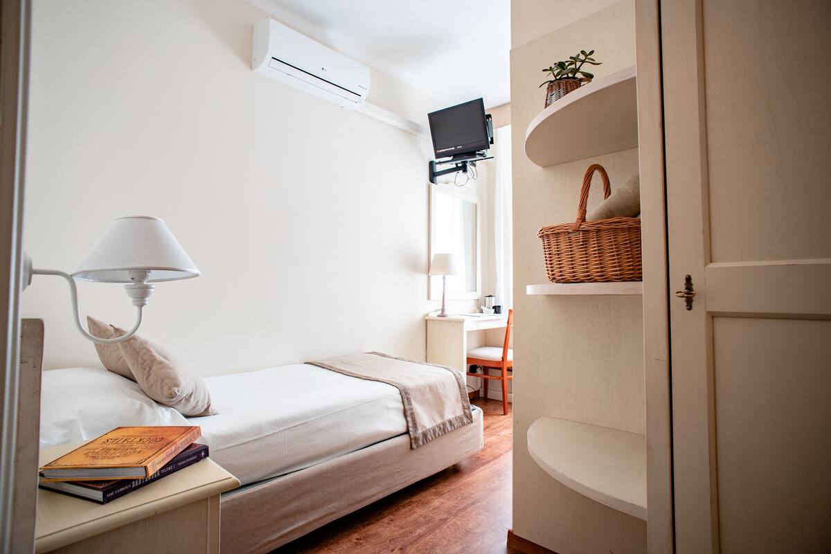 A bedroom with a bed, bedside table, lamp, and a desk with a chair.