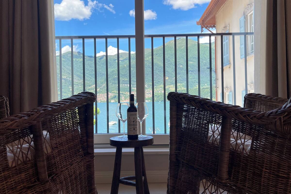 A balcony with wicker chairs, a table with a bottle of wine, and a view of a mountainous landscape.