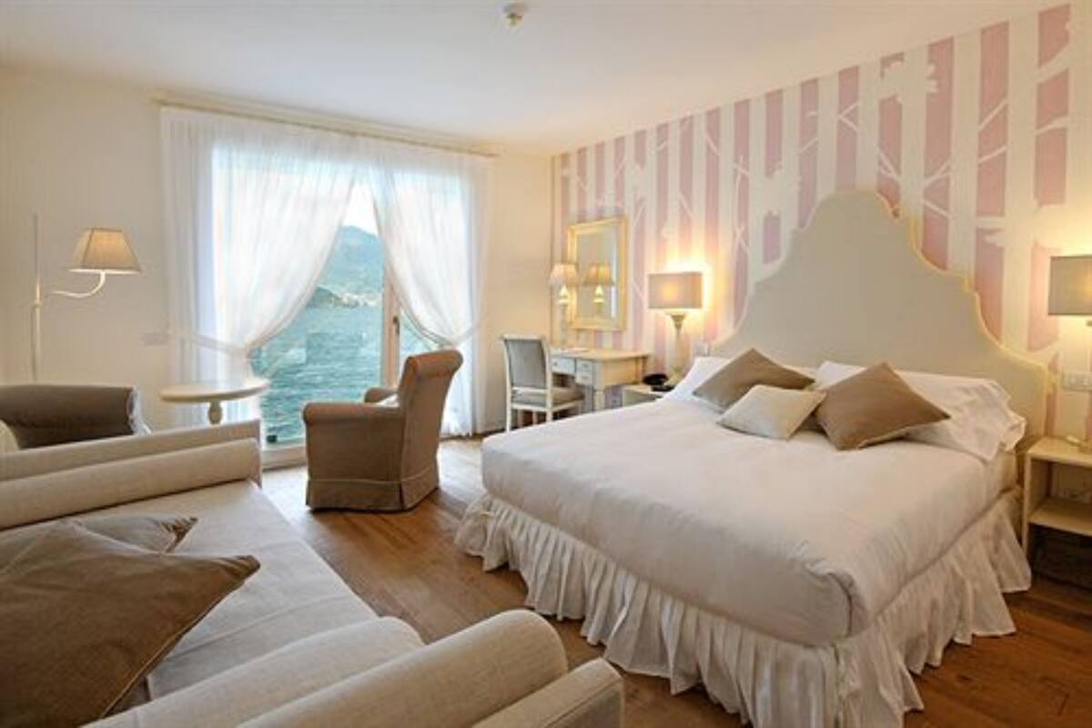A hotel room with a large bed, a sofa, a chair, a desk, and a view of the sea.