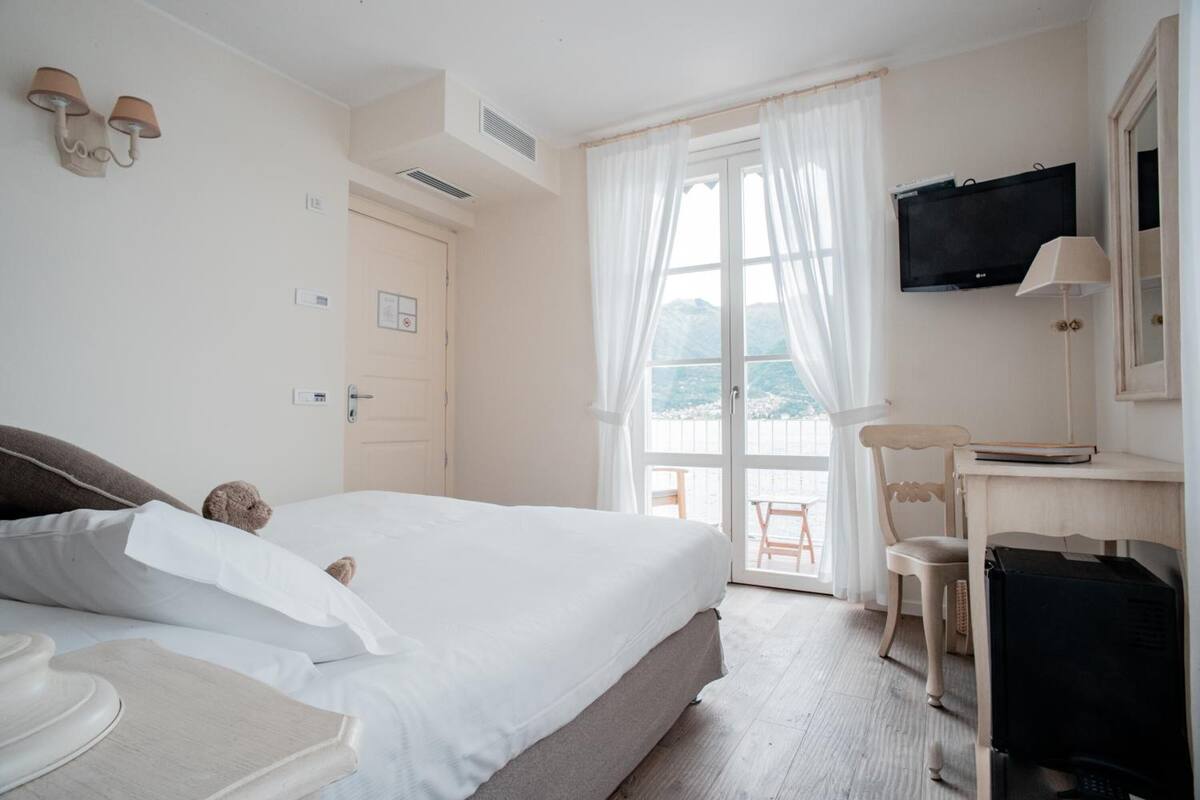A hotel room with a bed, a desk, a television, and a view of the outdoors.