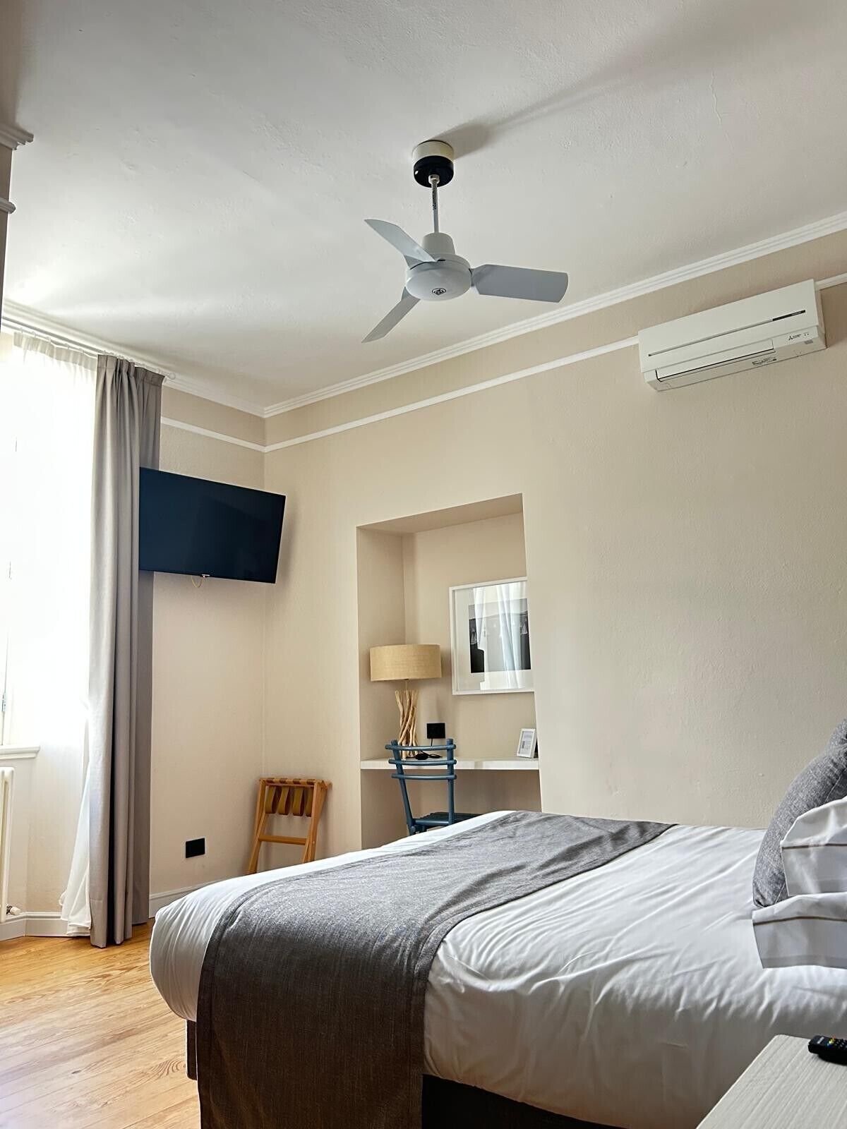 Une chambre d’hôtel comprenant un lit, un ventilateur de plafond, un téléviseur fixé au mur, un bureau avec une lampe et une chaise.
