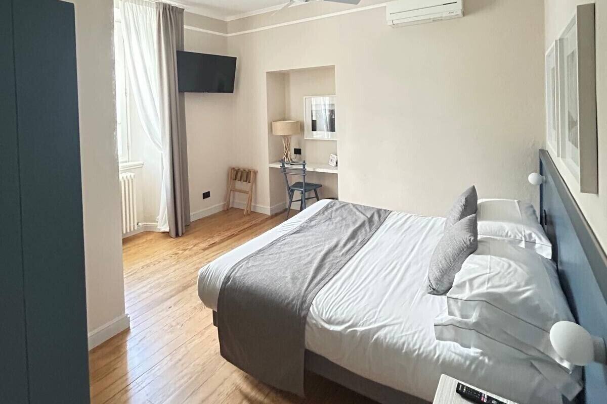 A bedroom with a bed, a desk, a chair, a ceiling fan, and a TV mounted on the wall.