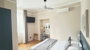 Un dormitorio con cama, escritorio, silla, ventilador de techo y televisor montado en la pared.