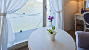 A room with a large window, a small table with a vase of flowers, and a lamp on a bedside table. - Hotel Villa Aurora (Lezzeno)