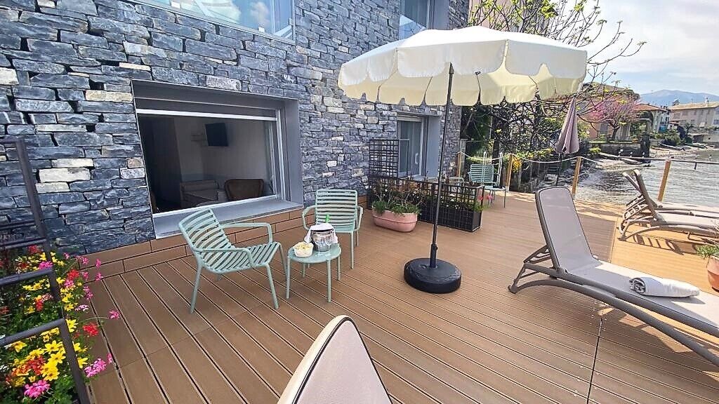 Une terrasse en bois avec des sièges d’extérieur, un mur en pierre et une vue sur l’eau.