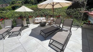 A patio with outdoor furniture, including lounge chairs and a sofa, under a large umbrella.