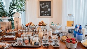 A breakfast buffet with various food items and beverages, a chalkboard sign with a message, and a potted plant. - Hotel Villa Aurora (Lezzeno)