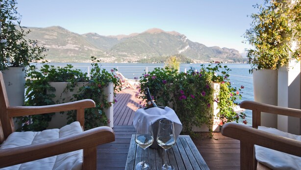 A wooden deck with two chairs and a table, a bottle, and two glasses of white wine. - Hotel Villa Aurora (Lezzeno)
