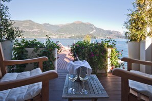 A wooden deck with two chairs and a table, a bottle, and two glasses of white wine.