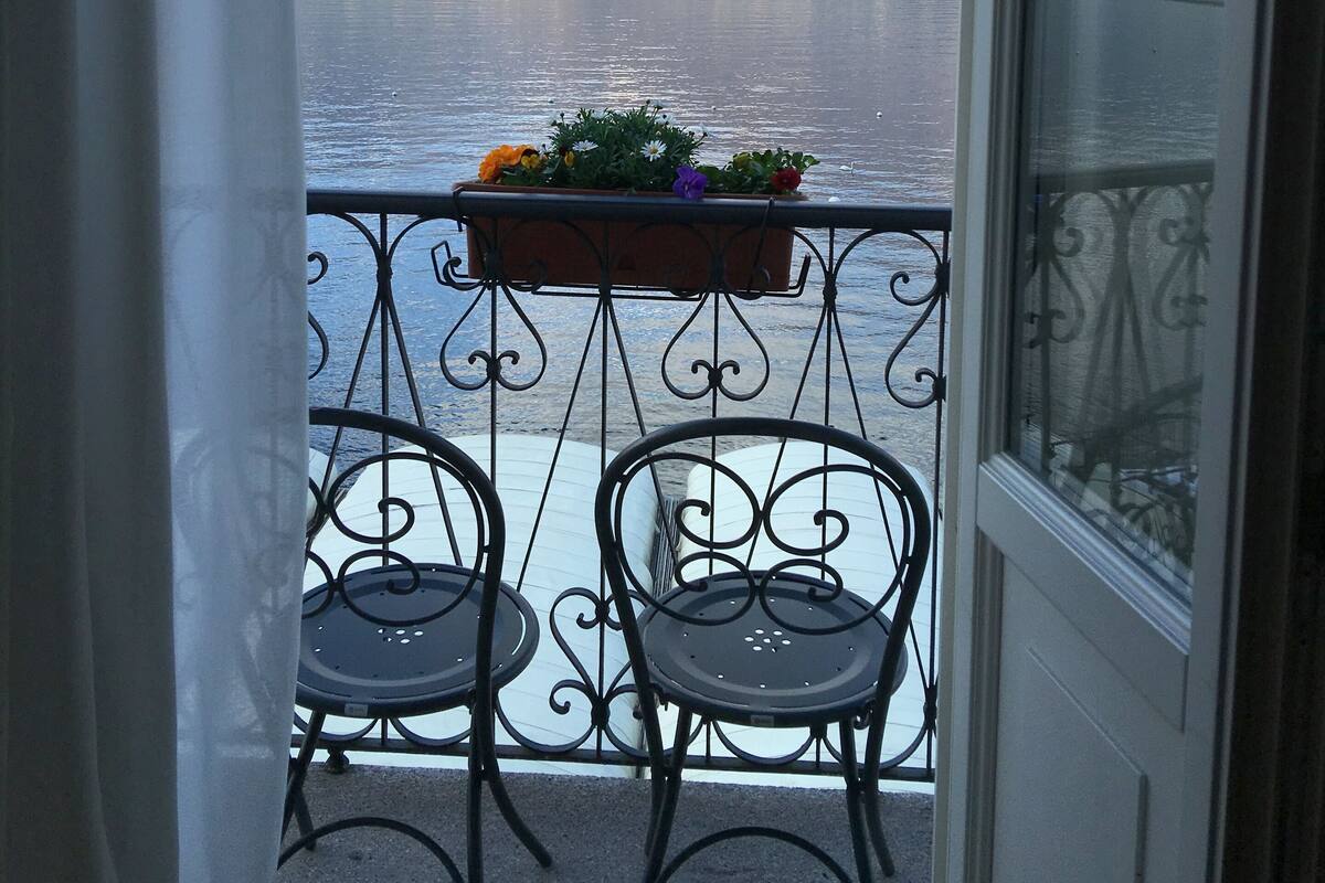 A balcony with two chairs and a flower planter, overlooking a lake and mountains.