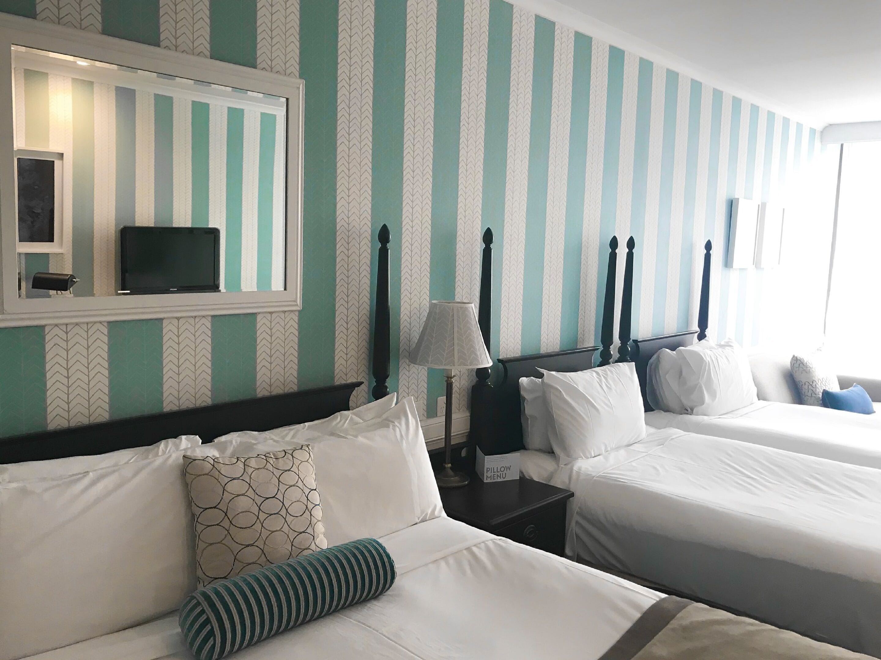 A hotel room with two beds, a TV, a nightstand, and a pillow menu.
