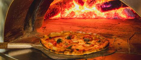 Una pizza dentro de un horno de leña con llamas visibles.