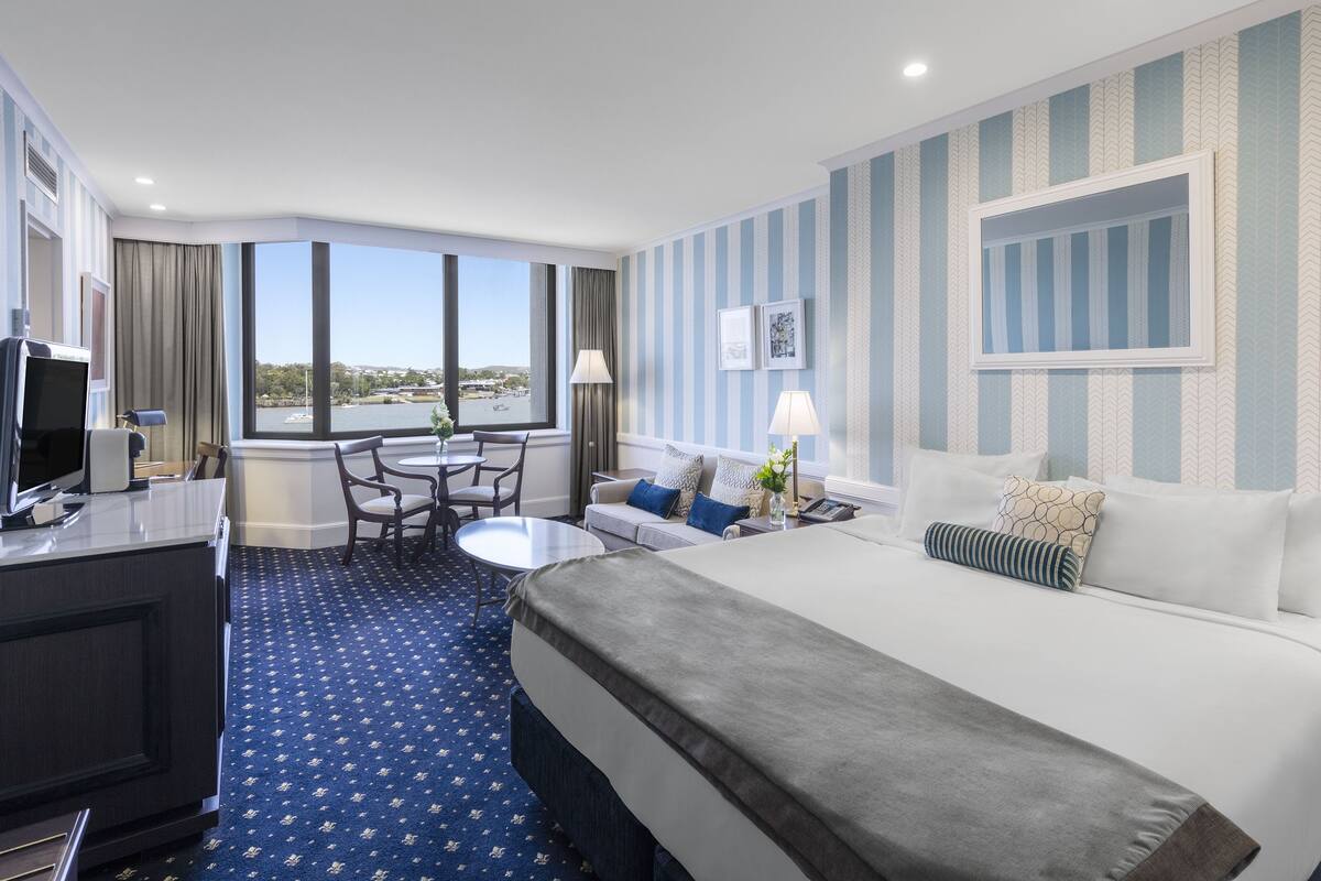 A hotel room with a large bed, a desk with a computer, a small table, and a view of the city.