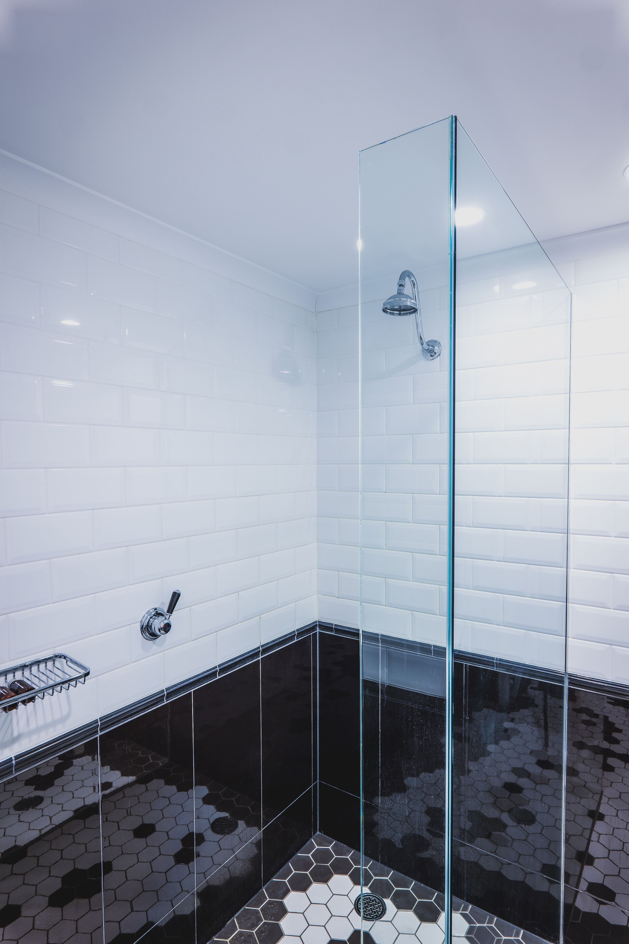 A modern bathroom with white tiled walls, a glass shower enclosure, and a black and white patterned floor.