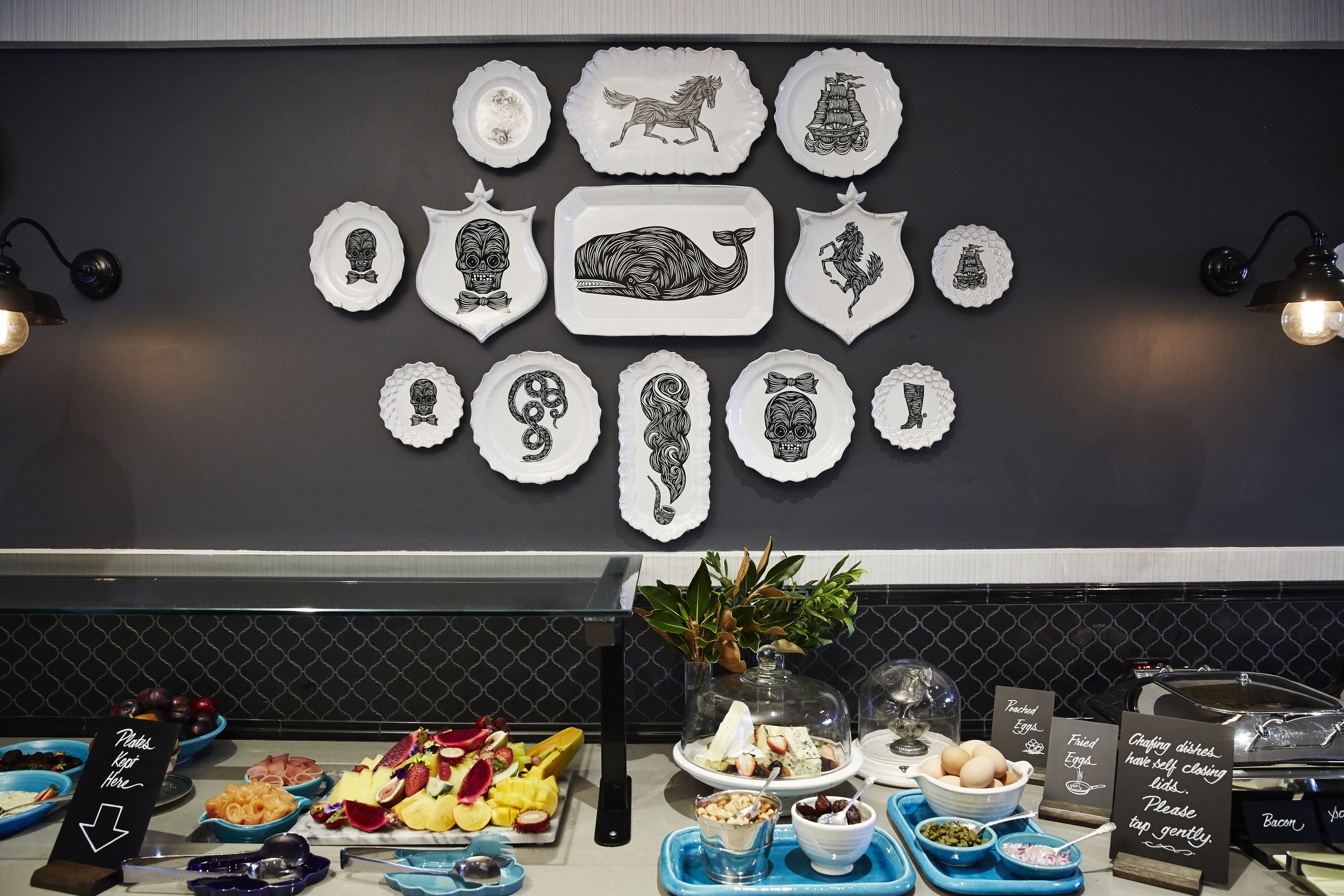 A buffet setup with various food items and a decorative wall with black and white plates.