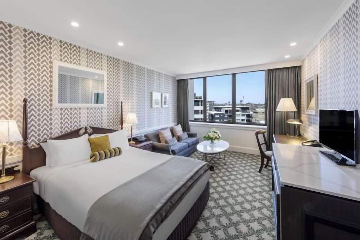 A hotel room with a bed, sofa, TV, and a large window with a city view.