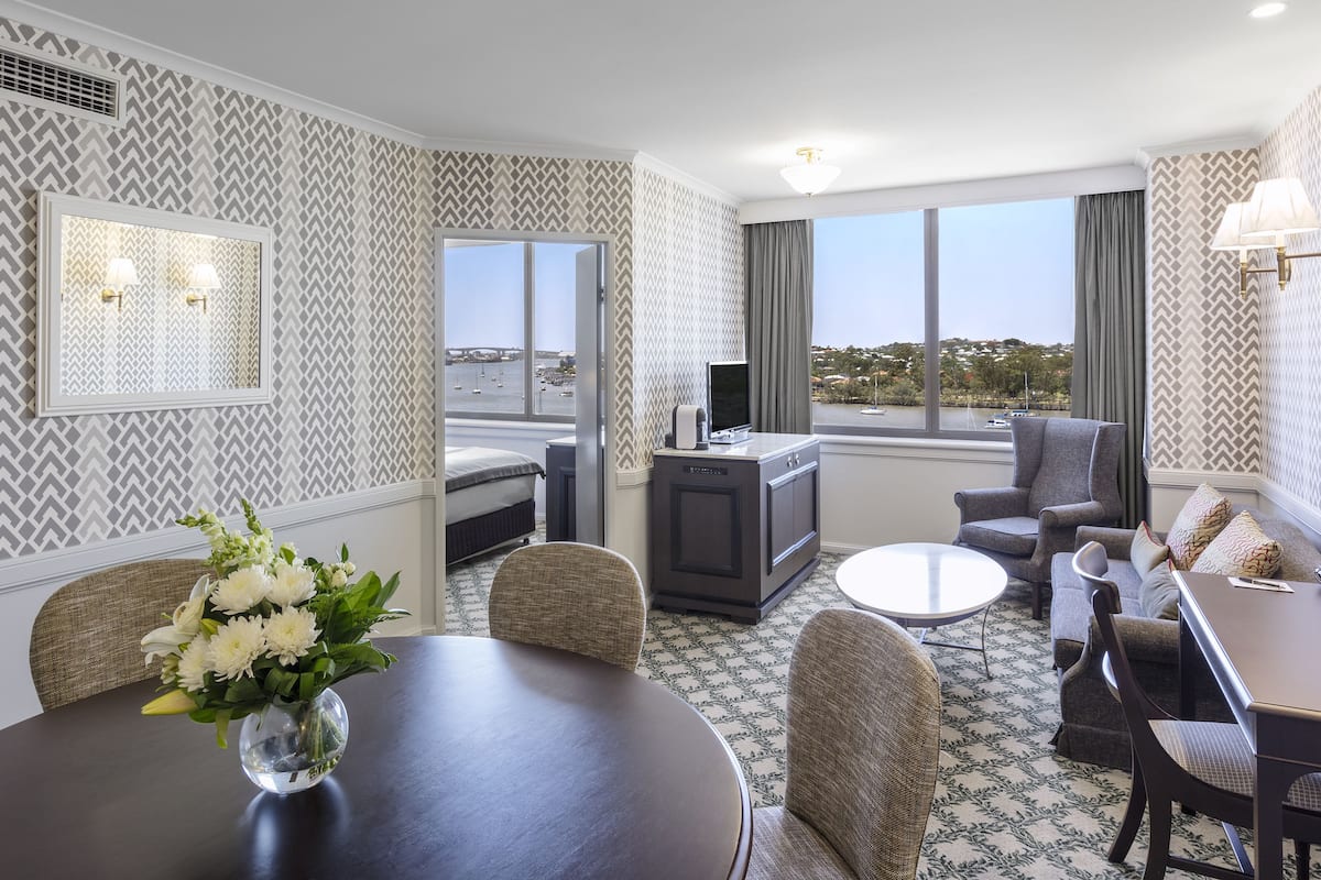 A hotel room with a dining area, a sofa, a TV, and a view of the city.