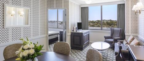 A hotel room with a dining area, a sofa, a TV, and a view of the city.
