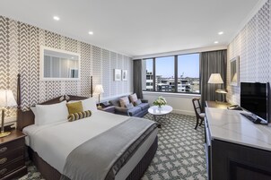 Una habitación de hotel moderna con una cama grande, un sofá, una mesita redonda y un televisor.