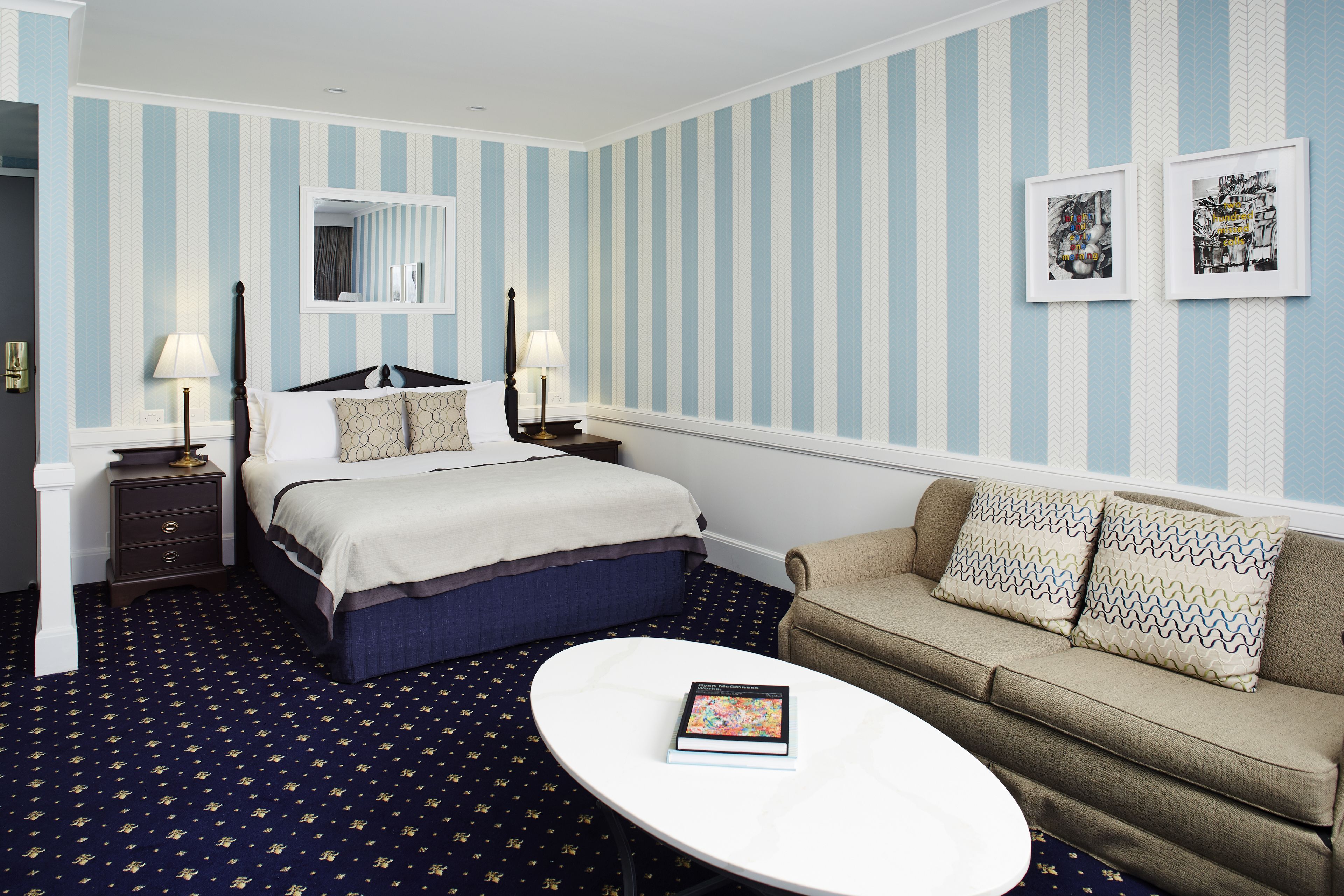 Une chambre d’hôtel avec un lit, un canapé, une table de chevet, une lampe et un livre posé sur une table.