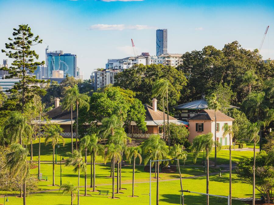 A park with a building, trees, and a city skyline in the background.