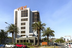 Un moderno edificio de hotel con un llamativo letrero 'VIEW HOTELS', palmeras y cielo despejado.