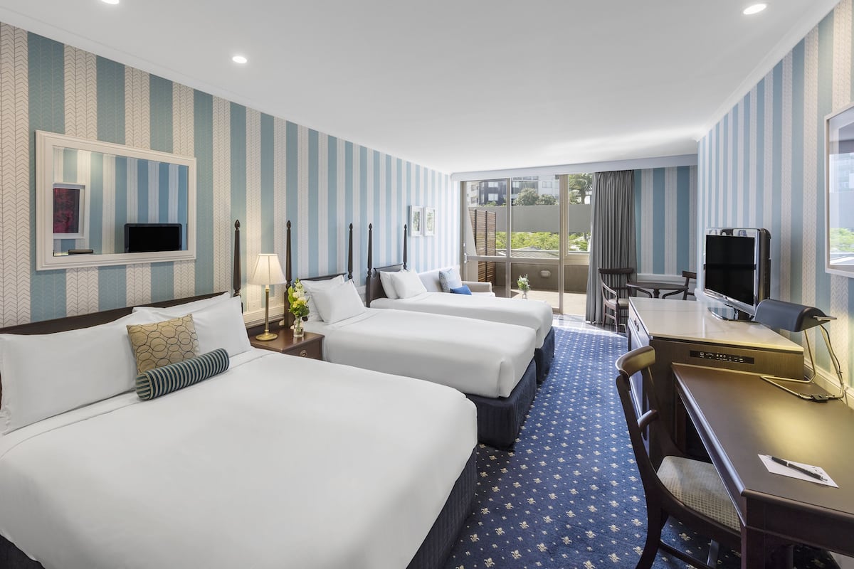 A hotel room with two beds, a desk, a chair, a TV, and a balcony with a view.