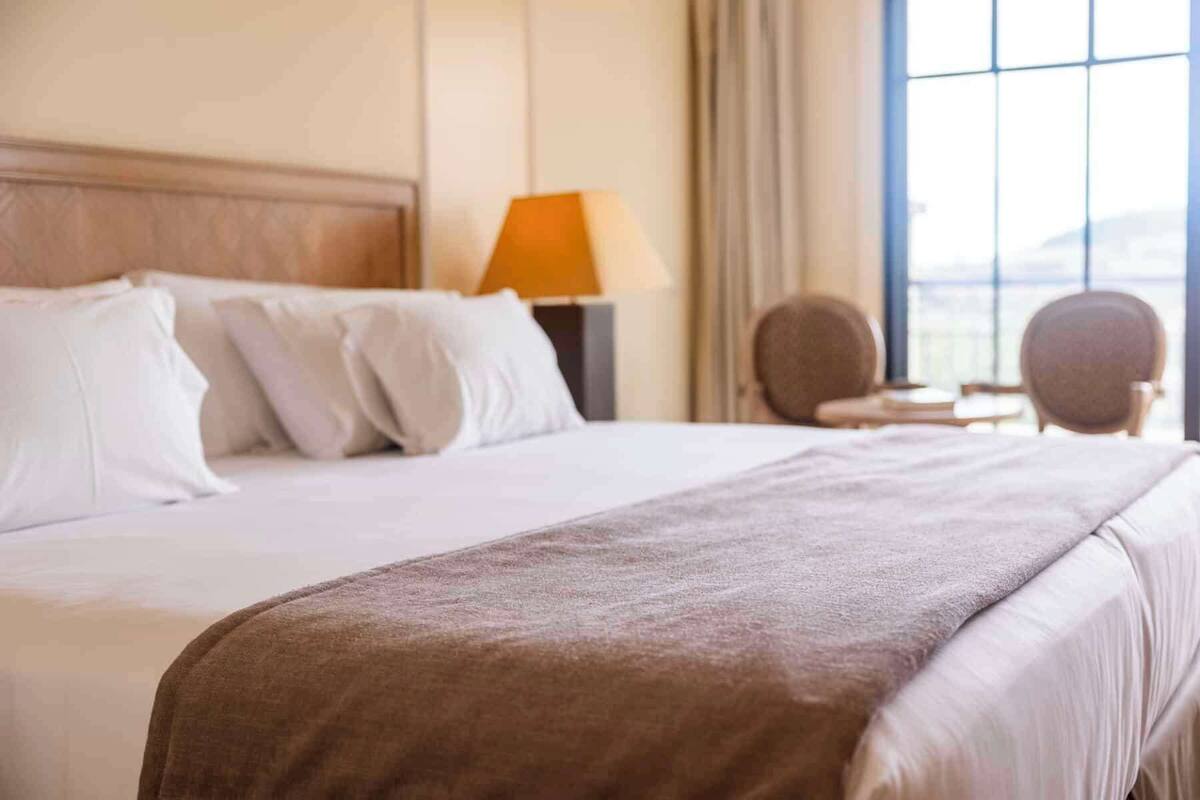 Une chambre d’hôtel avec un grand lit, une table de chevet avec une lampe et une vue sur l’extérieur par une fenêtre.